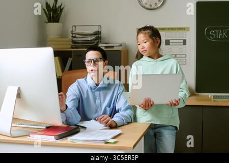 Middle Aged Caucasian Woman Teaching Asian Girl Using Computer and Laptop Stock Photo