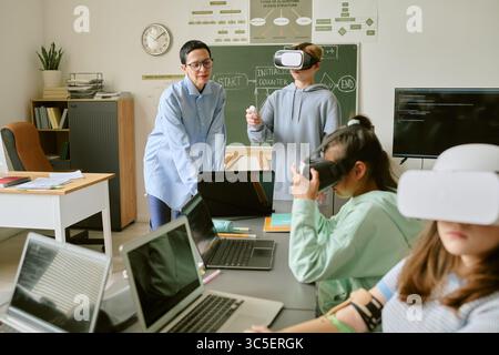 Teenagers and Caucasian Woman Teacher Using Virtual Reality Headsets in Classroom Stock Photo