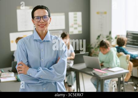 Portrait of Middle Aged Caucasian Woman Smiling in Classroom with Students Working Stock Photo
