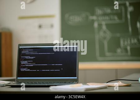 Laptop Displaying Programming Code in Classroom with Chalkboard in Background Stock Photo