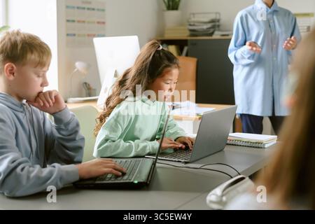 Asian Preteen Girl Using Laptop While Studying in Classroom with Classmates Stock Photo