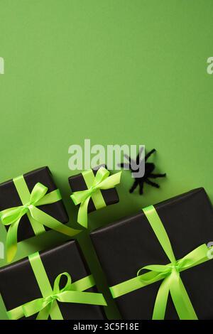 Halloween gift boxes with green ribbons on black wrapping paper, set on green background. Black fluffy spider. Space for your text. Stock Photo