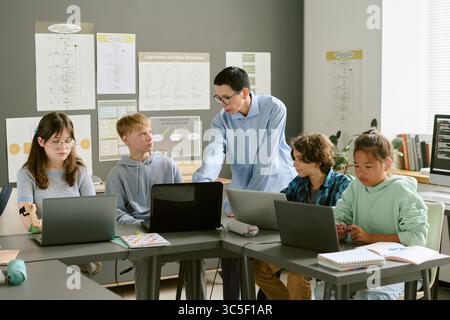 Teacher Instructing Diverse Teenagers Using Laptops in Classroom Stock Photo