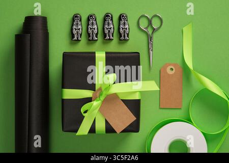 Halloween gift wrap with skeleton figures, black paper and neon green ribbon on a green background. Holiday preparation. Stock Photo