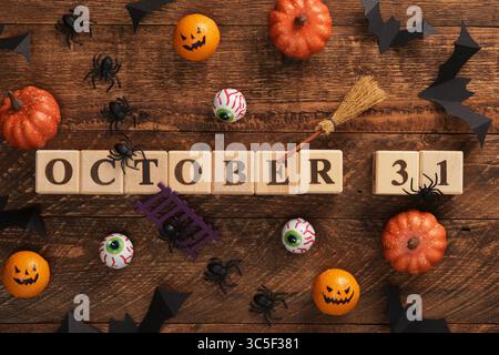 Text 31 October written with wooden cubes. Halloween vibes, pumpkins, eyes, bats, spiders, witch's broom. Stock Photo