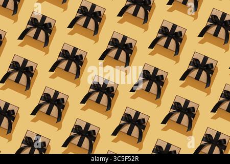 Elegant gold coloured gift boxes with black bows on a yellow background. Festive pattern. Stock Photo