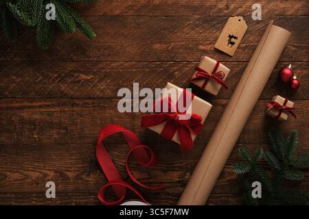 Gift wrapping items, roll of brown kraft paper, red velvet ribbon, labels on brown wooden table. Space for your text. Stock Photo