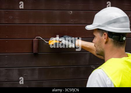 worker with paint roller painting wooden house exterior. wood protection, siding color restoration Stock Photo