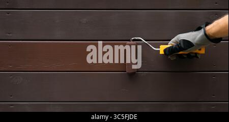 hand with paint roller painting wooden house exterior siding with protective color. wood protection. banner with copy space Stock Photo
