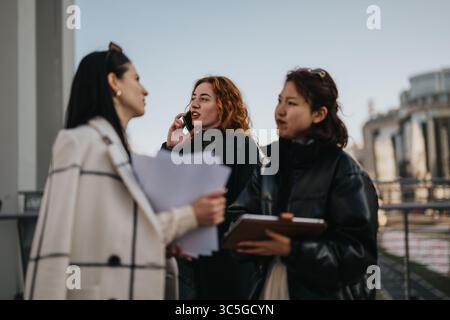 Three Women Collaborating Outdoors with Documents and Communication Tools Stock Photo