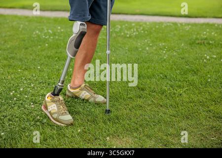 Man amputee with prosthetic leg disability on above knee transfemoral leg prosthesis artificial device on grass outdoor. People with amputation disabi Stock Photo