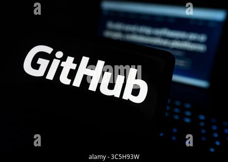 GitHub Logo Displayed On Computer Screen With Code Repository Open In Background Stock Photo
