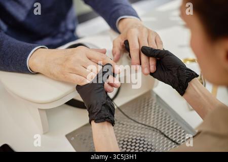 Caucasian middle aged man receiving manicure from young adult woman wearing black gloves, hands resting on table, close up of hands showing profession Stock Photo