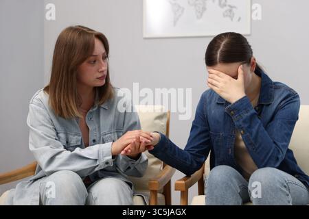 Woman apologizing to her offended friend on armchair near grey wall at home Stock Photo
