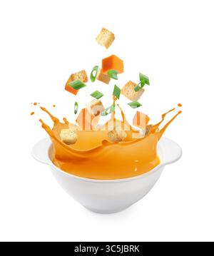 Croutons and pumpkin cubes falling into bowl of soup against white background Stock Photo