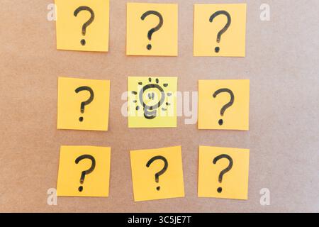 illuminated spotlight surrounded by question marks drawn on colored paper with black marker with a uniform solid background Stock Photo