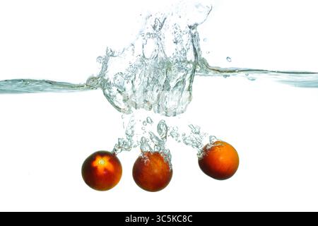 Dramatic splash of fresh red tomatoes submerged in clear water, creating dynamic bubbles and ripples against a white background. Stock Photo