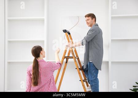 Couple putting painting on wall using ladder at home Stock Photo