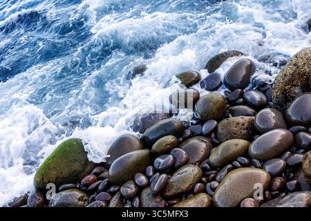 A wave with white foam and splashes running onto the coastal large pebbles. Turquoise water of the Atlantic Ocean. High quality photo Stock Photo