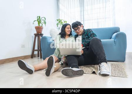 Young latin couple using laptop at home: woman with disability and prosthetic leg surfing the internet with husband Stock Photo