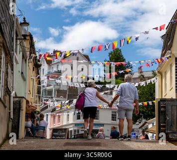 Older couple holding hands while walking down a charming street adorned with colorful bunting on a sunny day at Salcombe Devon Stock Photo