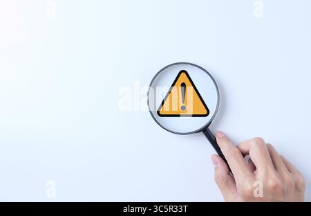 Warning alert system concept. Magnifying glass focused on yellow triangle warning sign. notification error and maintenance, cybercrime and virus, Mali Stock Photo