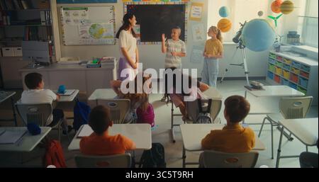 STEM Class on Renewable Energy: Elementary School Students Talking about Energy Sources in Front of Classroom Full of Classmates and Female Teacher. Diverse Children Studying Ecology and Science. Stock Photo