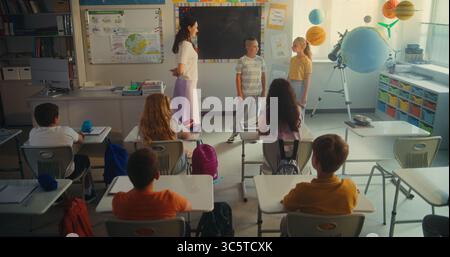 STEM Class on Renewable Energy: Elementary School Students Talking about Energy Sources in Front of Classroom Full of Classmates and Female Teacher. Diverse Children Studying Ecology and Science. Stock Photo
