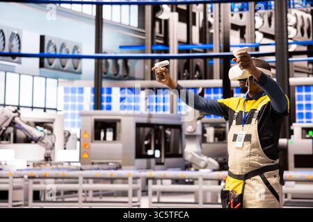 African American engineer with VR headset exploring industrial automation in smart manufacturing plant. Industry 4.0 specialist interacts with virtual reality simulation, improving system performance. Stock Photo