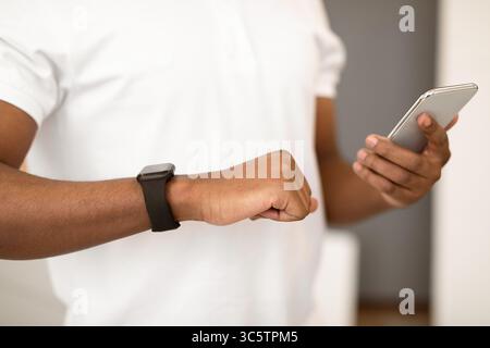 Unrecognizable Black Man Using Workout Gadgets Smartphone And Smartwatch Indoors Stock Photo