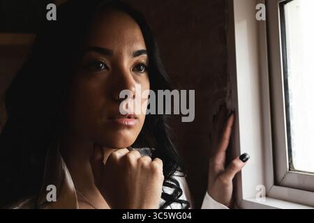 Young woman with hand on chin looking out window, contemplating Stock Photo