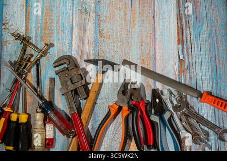 Different hand tools such as hammer, wrench, pliers, screwdriver, file, and screws lying on rustic wooden surface Stock Photo
