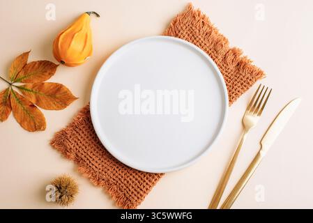 Empty round plate with pumpkin, autumn leaf and brown napkin on beige background. Top view, flat lay, mockup. Stock Photo