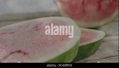 Displaying watermelon half slice showing red flesh with seeds and green rind on wooden board Stock Photo