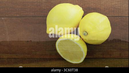 Displaying three bright yellow lemons resting on dark wooden tabletop, showing juicy interior pulp Stock Photo