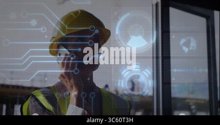 Talking supervisor wearing yellow helmet, vest at building site, holding smartphone with overlays Stock Photo
