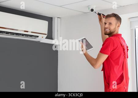 Male worker with tablet computer installing alarm system in room Stock Photo