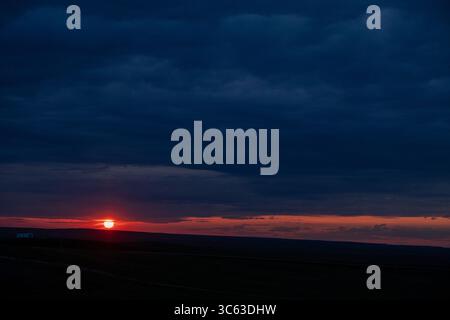 Sunset slips beneath dark storm clouds over the South Dakota plains, casting golden light across the vast prairie under a dramatic evening sky. Stock Photo