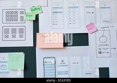 Mobile app wireframes and handwritten sticky notes covering wall, showing user interface design process with sketches, feedback notes, and layout planning for digital project Stock Photo