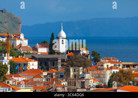 Funchal charming skyline features tiled rooftops, church tower, and greenery set against Atlantic Ocean. Scenic blend of architecture and nature Stock Photo