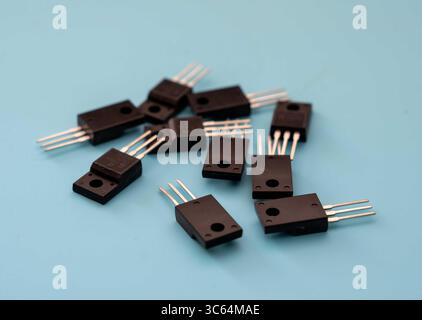 Close-up image of several black electronic transistors with three metal pins each, scattered on a blue background. Ideal for illustrating electronic c Stock Photo