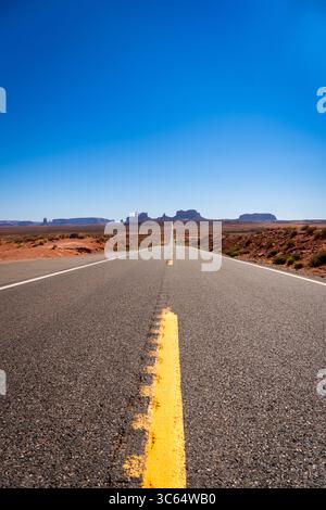 Vertical view of a long road stretches through the desert, marked by a yellow line,in the main road of Monument Valley, USA Stock Photo