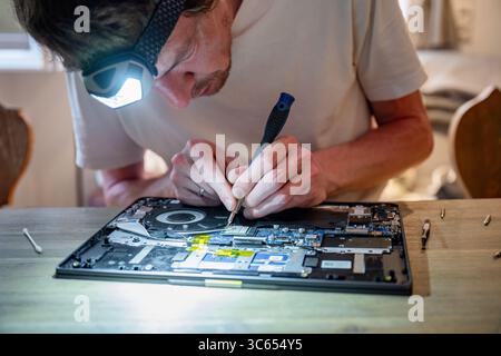 Man repairing laptop with tools on table, computer maintenance concept Stock Photo