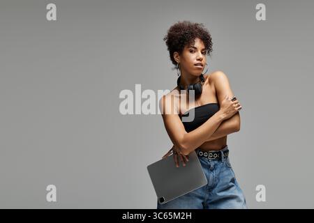 Curly haired woman showcases fashionable style while holding a gadget in a modern setting. Stock Photo