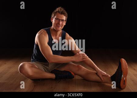 young man doing floor training, stretching, black background Stock Photo