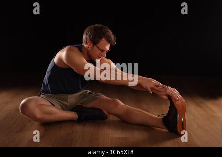 young man doing floor training, stretching with hand, black background Stock Photo
