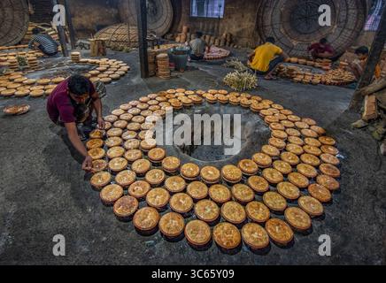 Bogura, Bangladesh - 03 May 2020: View of workers meticulously arranging fresh, golden-brown, circular food items around a central opening in a rustic, dimly lit industrial setting. Stock Photo