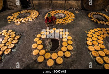 Bogura, Bangladesh - 03 May 2020: View of a worker meticulously arranging golden-hued, circular cakes around dark, soot-stained pits in a rhythmic, repetitive pattern. Stock Photo