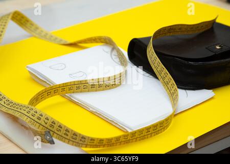 A bright yellow measuring tape is laying on top of a notebook Stock Photo
