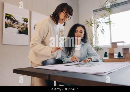 Two colleagues engaged in a collaborative planning session, discussing architectural drawings in a creative environment. Teamwork, project management, Stock Photo